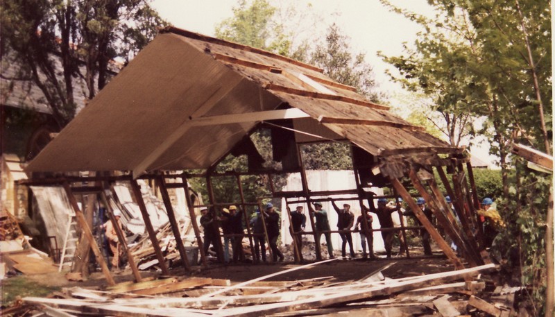 Photo of the demolition of the Tin Tab, with the walls removed and the structure apparently in the process of being pushed over by volunteers