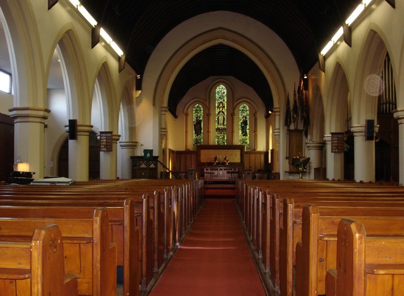 Photo of the church interior prior to the re-ordering, the view is up the central aisle towards the chancel and east wall, pews visible either side of the aisle