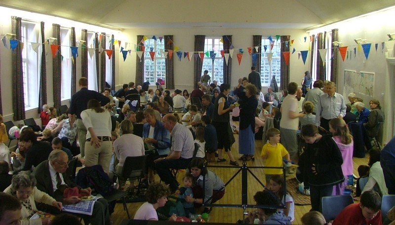 Photo from the indoor picnic in the Parish Halls showing many CCNM members enjoying their picnic and conversation; red, white and blue bunting on display
