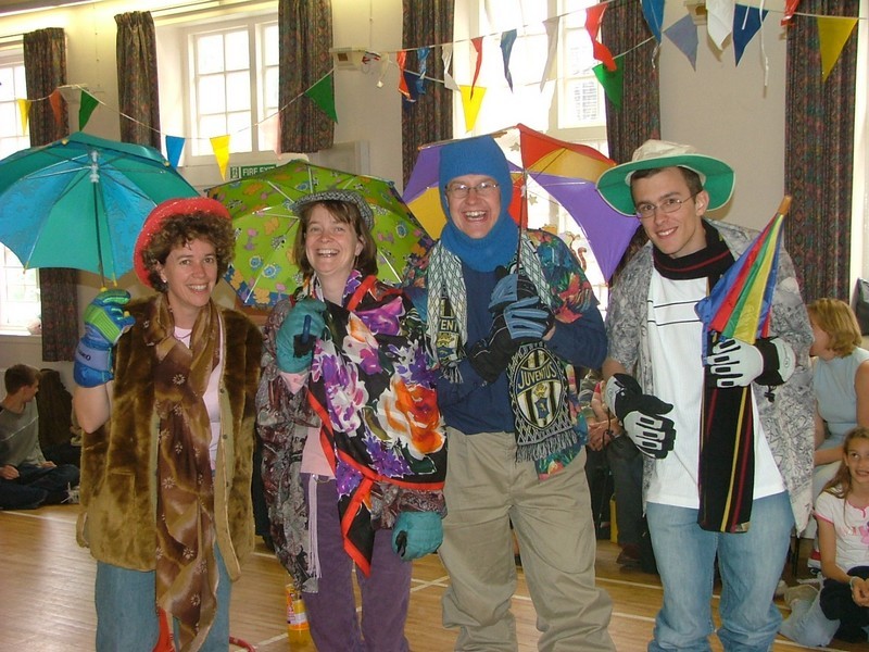 Photo from the indoor picnic on the upper floor of the Parish Halls, Helen Hancock, Sarah Parker and Stephen Kuhrt with umbrellas and dressed for cold and wet weather