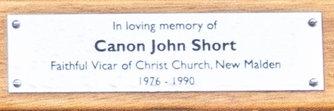 Close up of the plaque on the bench dedicated to John Short, which reads 'In loving memory of Canon John Short, Faithful Vicar of Christ Church New Malden, 1976 - 1990