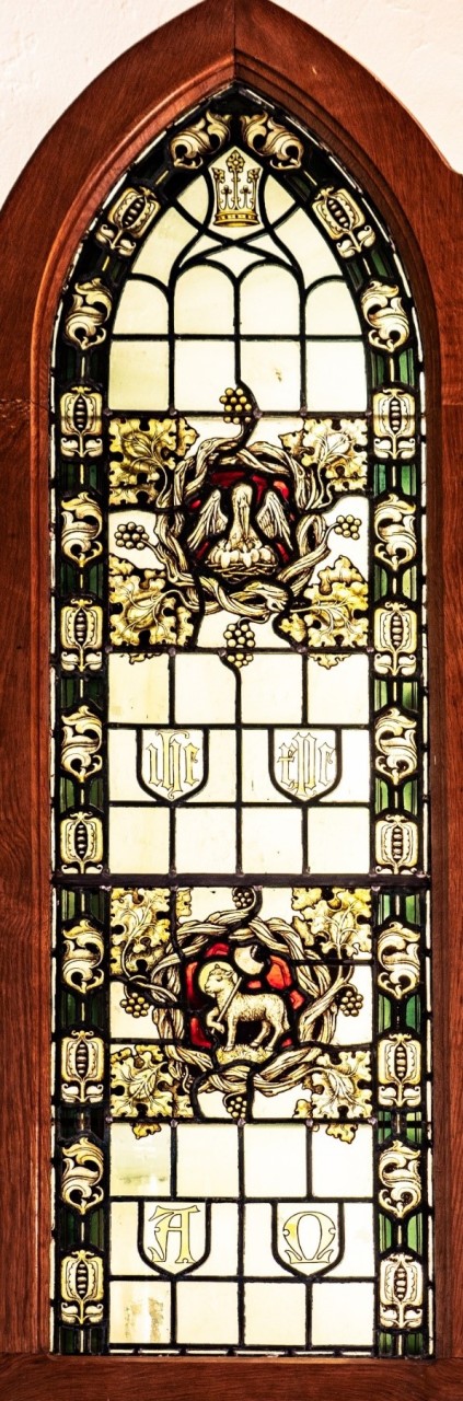 Photo of the Merryweather window; in the upper half a picture of a pelican feeding her chicks; in the lower half a lamb; below this the letters 'A' (Alpha) and Omega