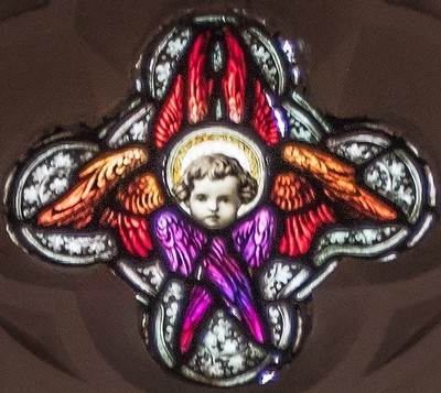 Photo of the upper part of the Simeon and Anna window featuring the face of a cherub at the centre surrounded by 4 pairs of folded wings 