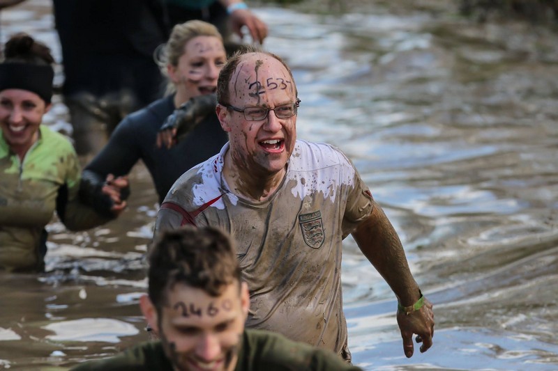 A wet and muddy Stephen Kuhrt wading through water during the Wolf Run, identified by the number 2537 written on his forehead